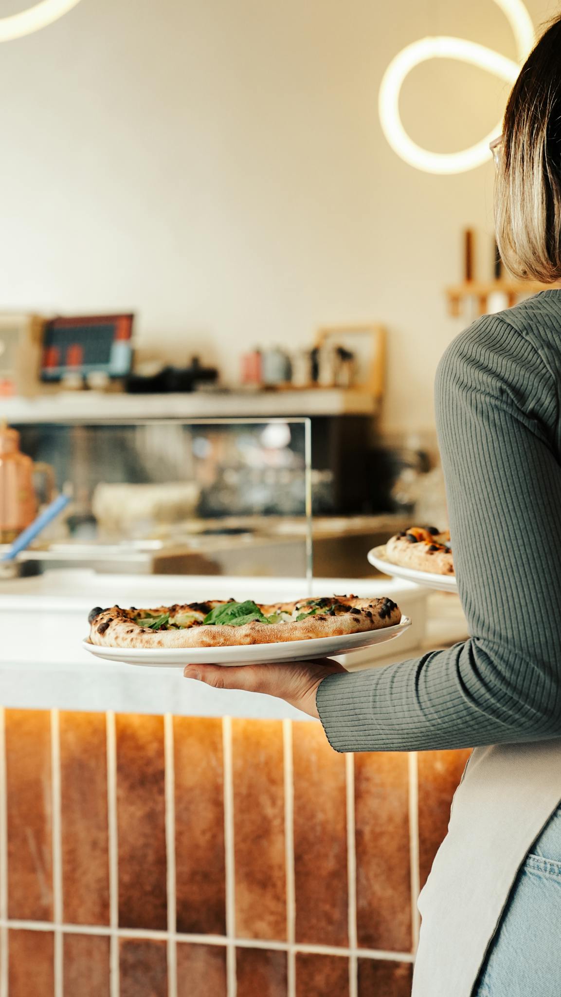 A waitress holding a plate of delicious pizza in a warm, cozy restaurant setting.