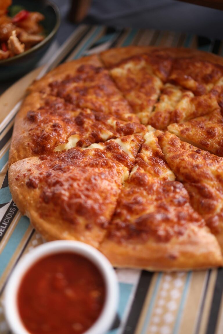 Close-up of a cheesy pizza with a side of tomato sauce, perfect for lunch or dinner.