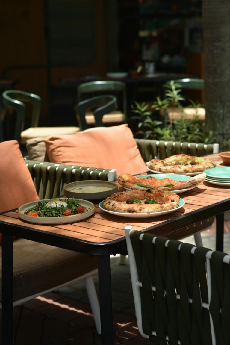Enjoy an appetizing outdoor meal with pizzas and salad on a sunny patio.