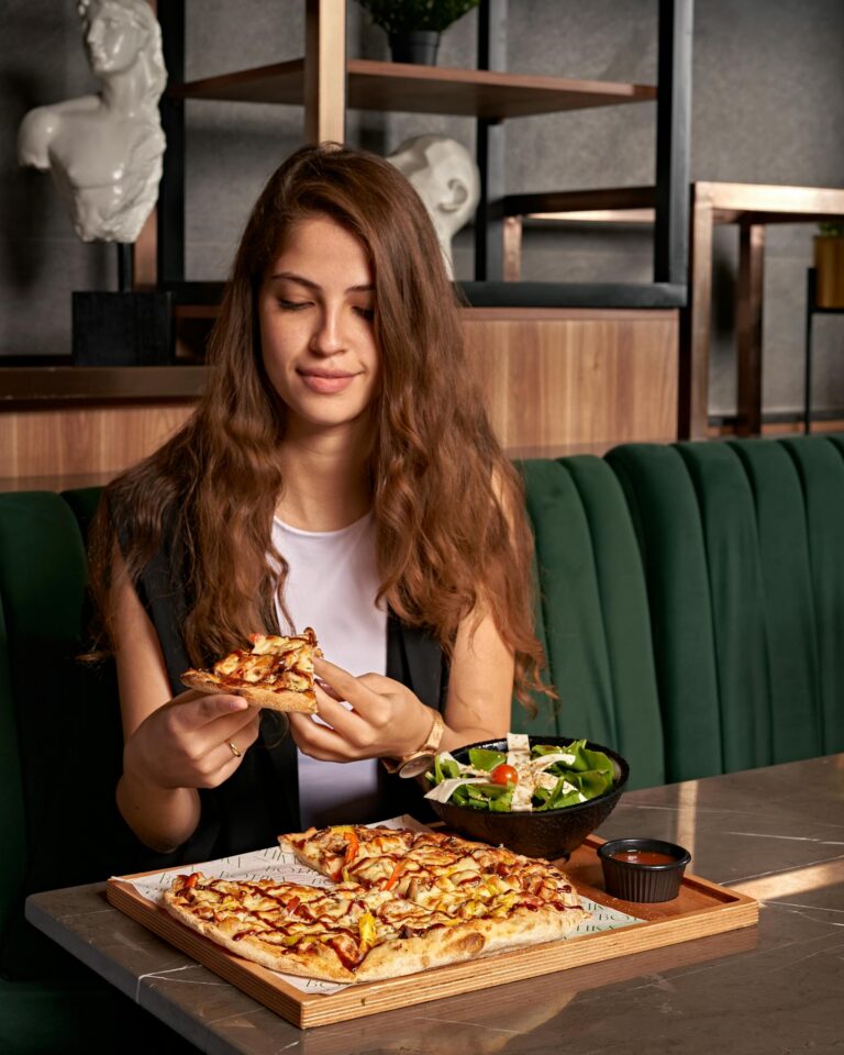 Young woman sitting at a cafe table, enjoying a slice of pizza with a fresh salad.